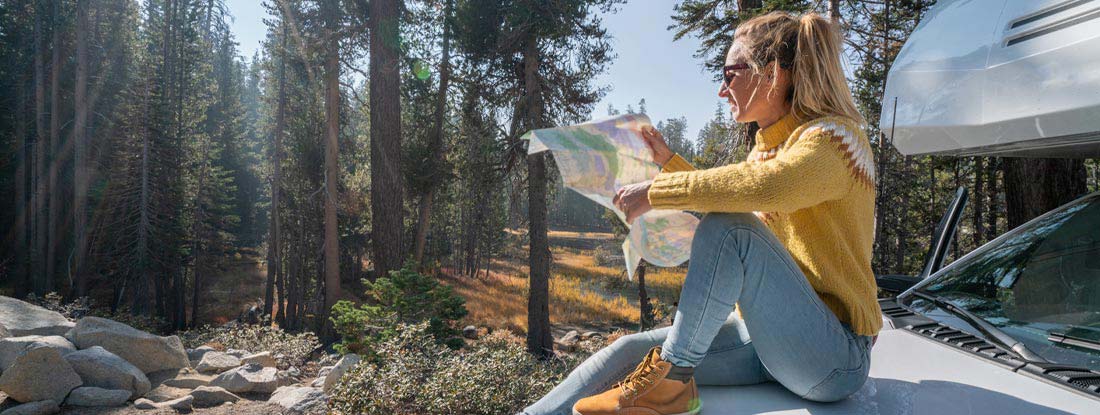 Woman sitting on motorhome hood checking road map for directions. Find Tennessee RV Insurance. 