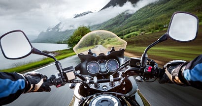 Biker rides a motorcycle in the rain. Find Motorcycle Insurance.