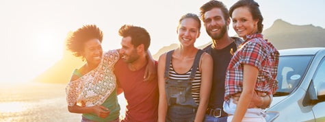 Group of teenage friends standing by car on coastal road