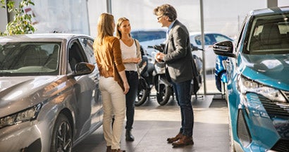 Female customers having a conversation with a salesman standing next to new cars at a car dealership. What is the best time to buy a car?