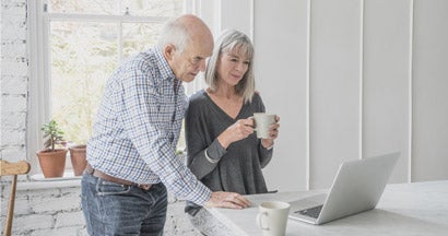 A senior man and his wife are looking at a laptop computer together. Pros and cons to long term care insurance.