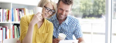 A couple drinks coffee while looking at a tablet computer.
