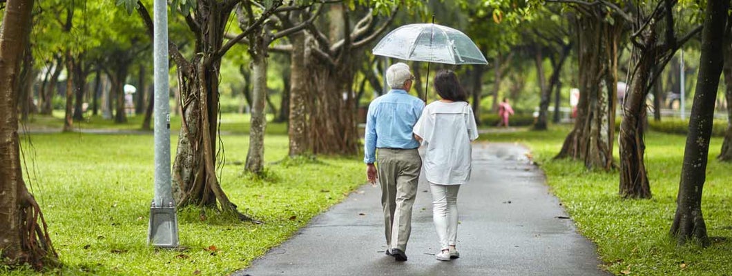 Couple Walking in park With Umbrella. Traditional long term care insurance.