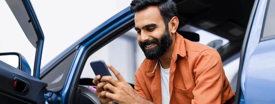 Man Using Phone Sitting In Auto With Opened Door. Is Car Insurance Always Required?