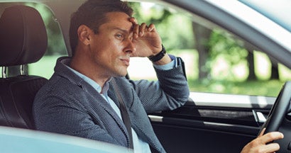 Frustrated businessman in a suit driving his car.  Simple signs you have the worlds worst insurance.