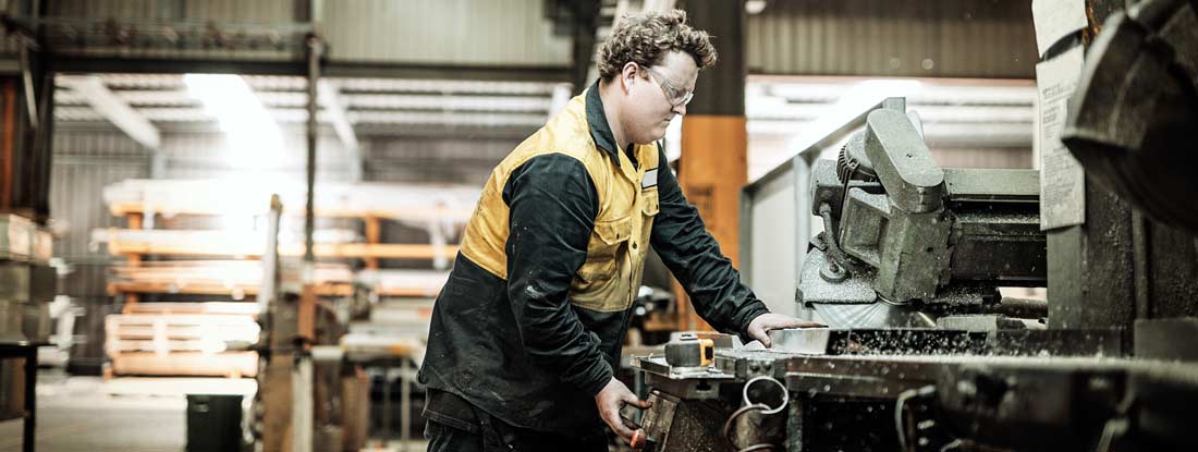 Blue collar worker in factory cutting metal parts. Workers' compensation for employees.