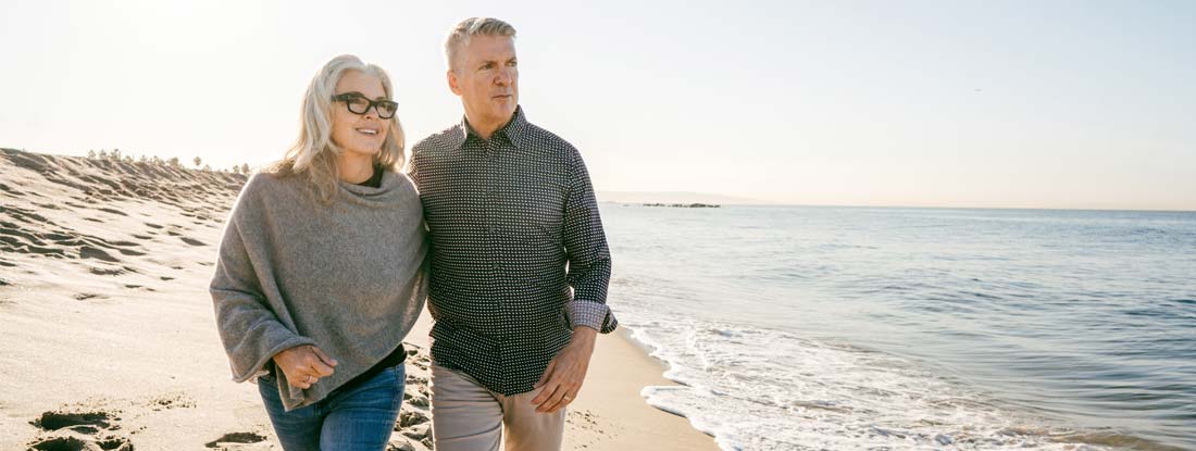 Mature couple walking along beach. Permanent Life Insurance Cost.