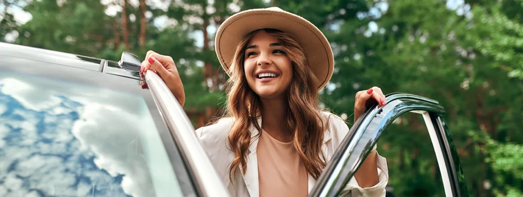 Woman in a hat stands near the car on the background of the forest. Find Woodstock, Georgia car insurance.