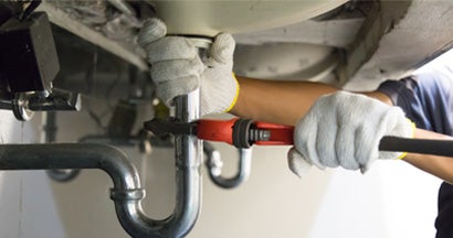 Plumber using a wrench to tighten a siphon under a sink. Find Home Repair Insurance.