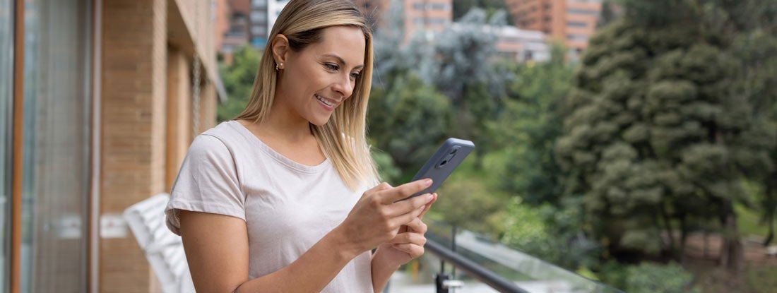 Woman using her phone from the balcony of her apartment. Find Wyoming renters insurance.