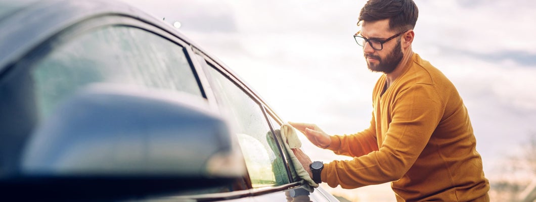 Young man cleaning the windows on his car outside. How to Find the Best Car Insurance in Madison, SD. 