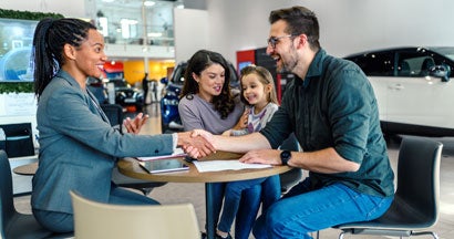 Happy family came to an agreement with a car salesperson at a meeting in a showroom. How to Get a Car Loan the Easy Way.