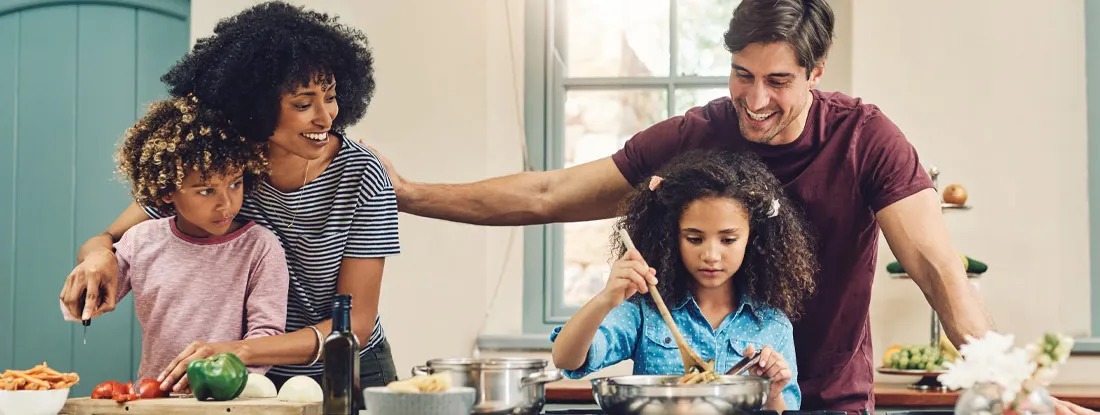 Family of four cooking together in their kitchen at home. Term vs. Permanent Life Insurance. 