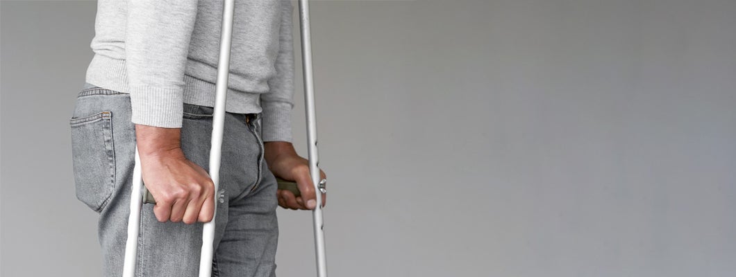 Man on crutches on a gray background. Disability income insurance programs in my state.