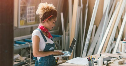 Carpenter standing in her workshop. Holding laptop while she focused on her work.