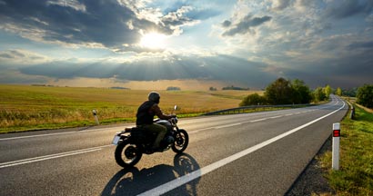 Person riding a motorcycle on a scenic country road. Find Motorcycle Liability Insurance.