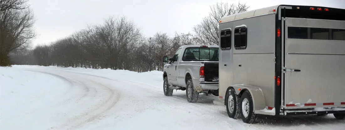 Pickup truck towing a horse trailer on a snow-covered road. Find Trailer Liability Insurance.