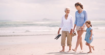 Generations of women, a grandmother, mother, and granddaughter, walking together on a beach. Buying life insurance for your parents.