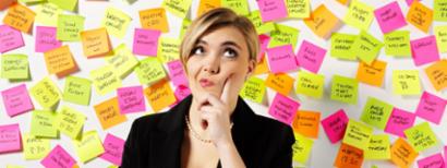 A woman stands in front of a wall of post-it note reminders, wondering.