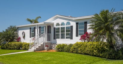 Mobile home landscaped with front lawn, palm trees and a clear sky. How mobile homes are insured.