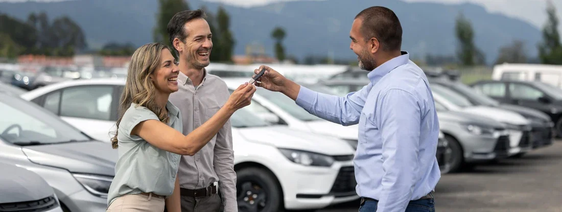 Salesman giving the keys of car to a couple at the dealership. Used Cars: What Are You Really Paying For?