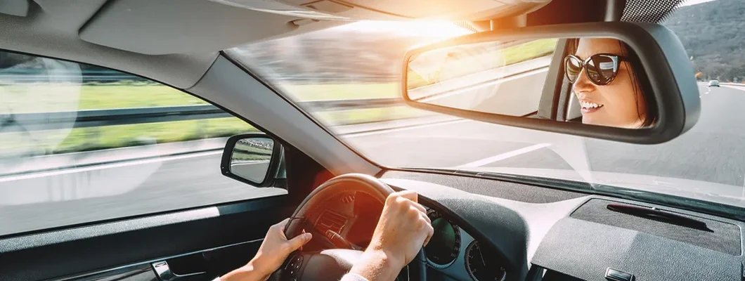 Woman driving a car reflects in back view mirror. How to Find the Best Car Insurance in Clayton, MO. 