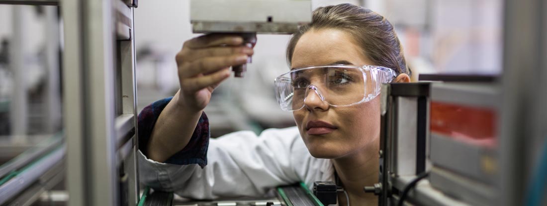 Female engineer examining machine part on a production line. Find engineering insurance.