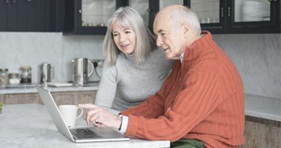 Senior man and woman using laptop at home together. Long term care insurance by state. 