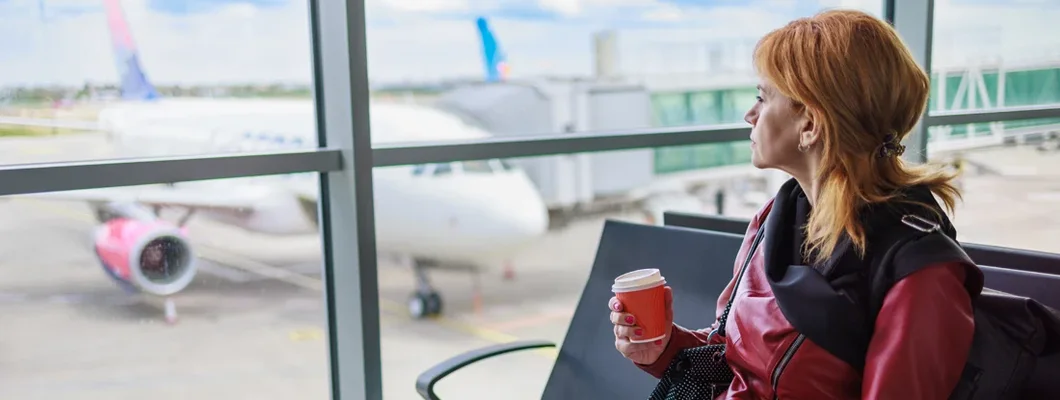Times When Travel Insurance Is a Must-Have. Woman sitting at the gate waiting room with traveling documents and coffee. 