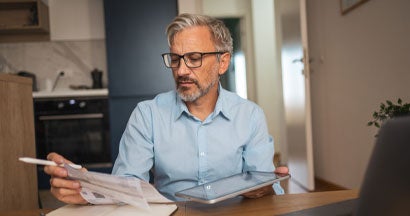 Man reviewing financial documents at home with tablet and laptop. How to Prevent Cybercrime.