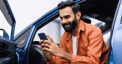 Man Using Phone Sitting In Auto With Opened Door. Is Car Insurance Always Required?