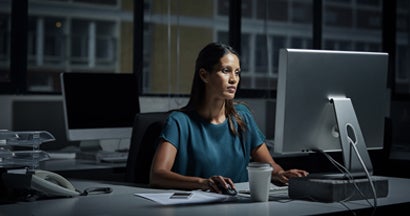 Businesswoman using computer in dark office.  Find Business Cyber Liability Insurance.