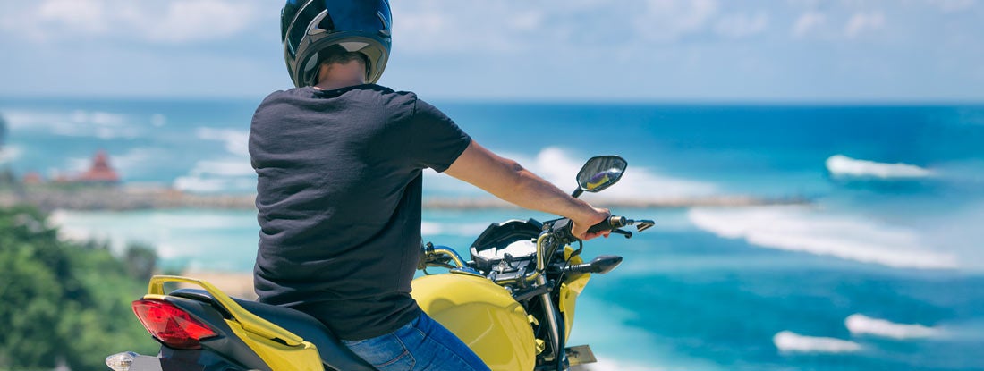 Man sitting on motorcycle on Hawaii beach. Find Hawaii Motorcycle Insurance.