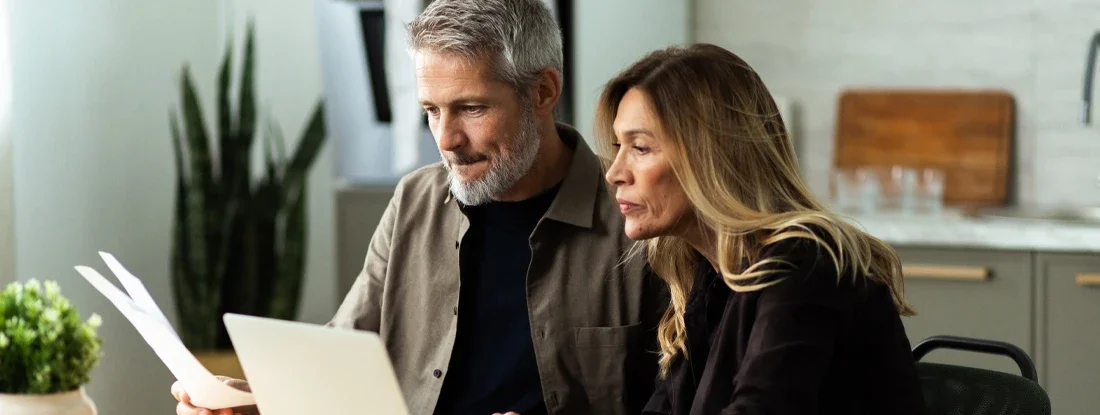 Couple planning home finances using laptop and documents. Supplemental Health Insurance.