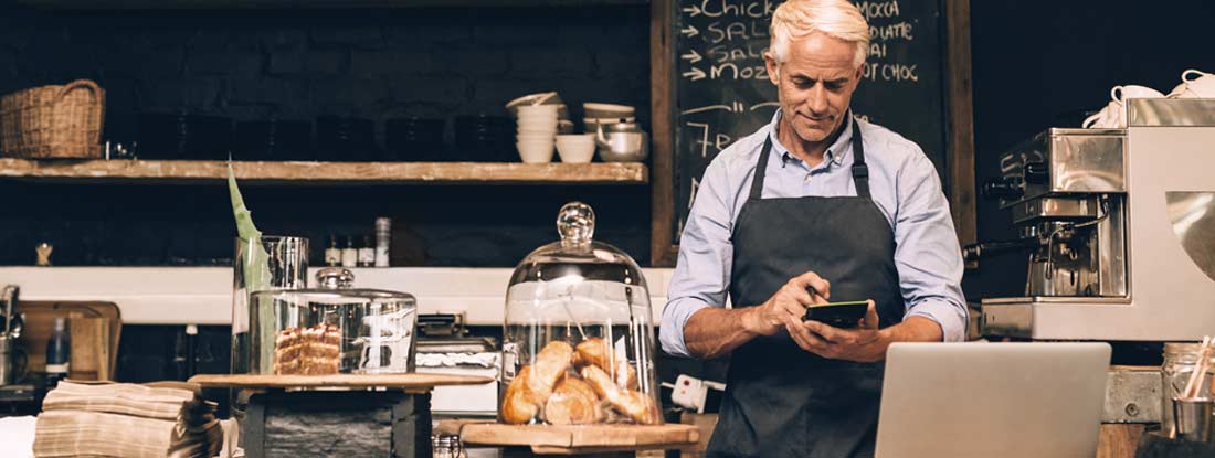 Man using a calculator behind his cafe counter. How to calculate workers' compensation.