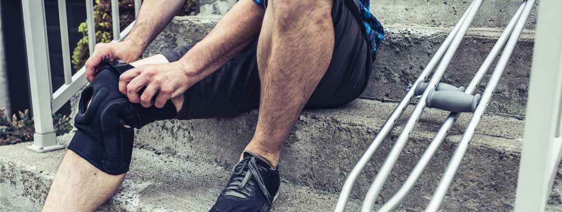 Man sitting on the steps and adjusting his orthosis after having knee sprain accident. Individual short term disability insurance cost.