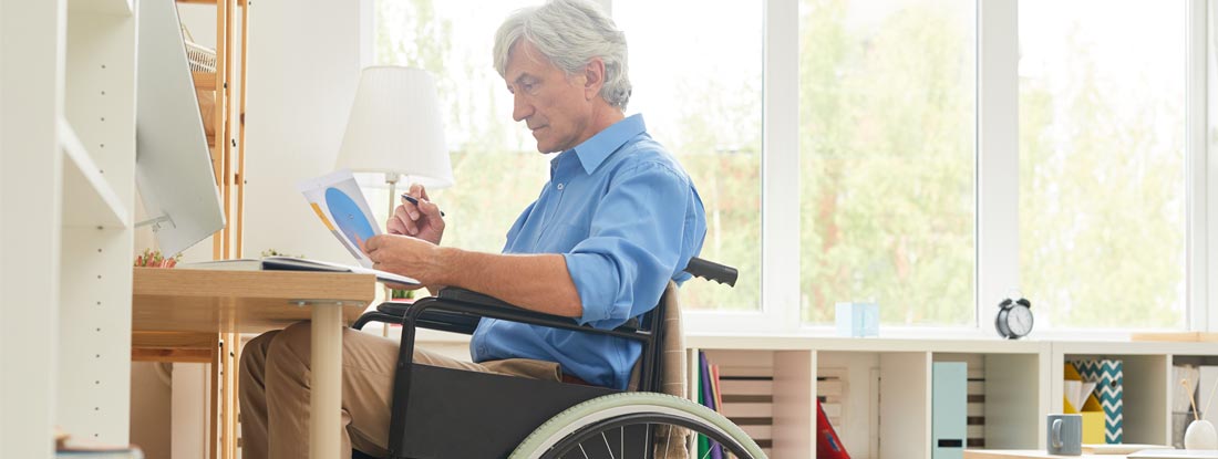 Disabled man sitting in wheelchair examining tax documents in front of computer. Is disability insurance taxable?