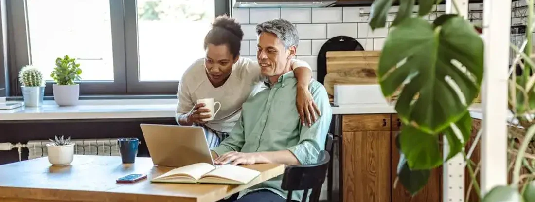 Man is working on the laptop and his wife is next to him. Compare Health Insurance. 
