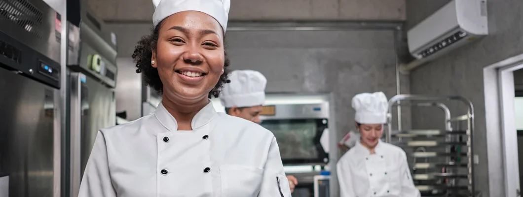 African American female chef looks at camera with a cheerful smile in a kitchen. How to Find the Best Business Insurance in Lenexa, Kansas.