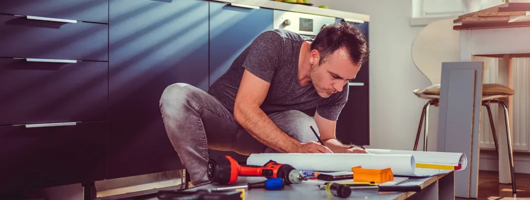 Man checking blueprints while building kitchen cabinets. 6 Major Home Renovations that Impact Your Homeowner’s Insurance Needs.