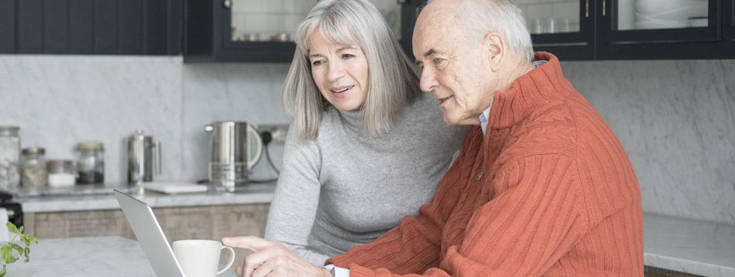 Senior man and woman using laptop at home together. Long term care insurance by state. 