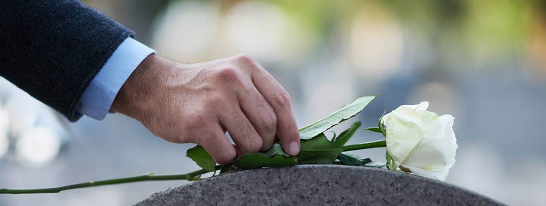 Hand placing a single white rose on a tombstone. Final Expense Insurance.