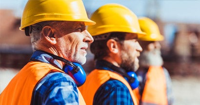 Builders in reflective vests and hardhats standing together at construction site. Find Licensed, Bonded and Insured Business Insurance.