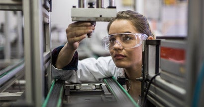 Female engineer examining machine part on a production line. Find Manufacturer's Insurance.