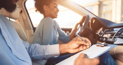 Young woman driving car, feeling inexperienced, instructor controlling and checking