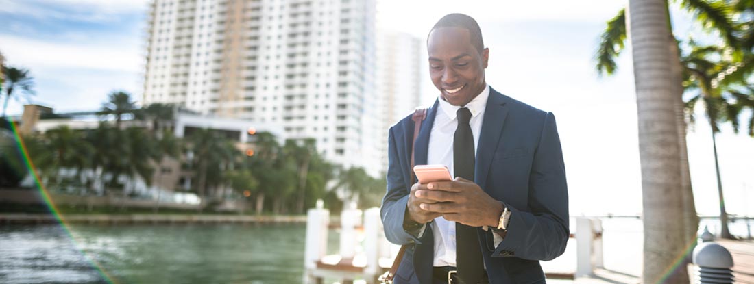 Professional in a suit looking at a mobile device near a waterfront. Find Miami business insurance.