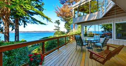 Wooden walkout deck with outdoor table set and swinging bench at lake house. Seven Essential Considerations Before Buying That Gorgeous Lake House.