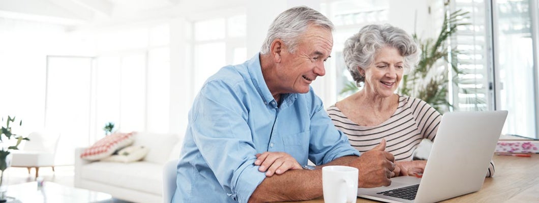 Senior couple happily using a laptop at a table. How does a fixed annuity work?