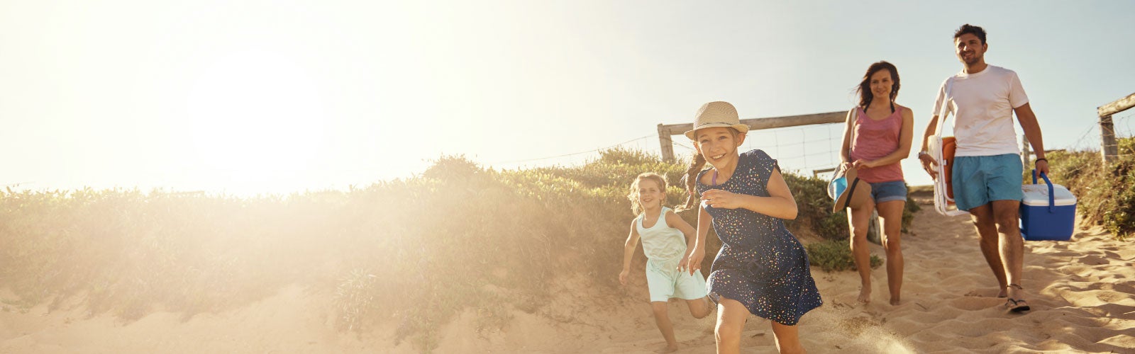 Family carrying a cooler and chair to the beach. Find Travelers insurance.
