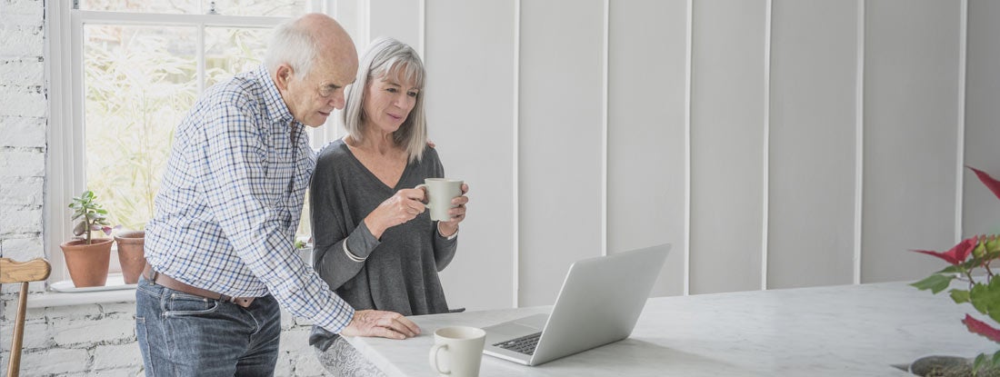 A senior man and his wife are looking at a laptop computer together. Pros and cons to long term care insurance.